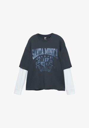 Tricou supradimensionat de culoare gri închis, cu grafică albastră "SANTA MONICA" și emblemă de leu, stratificat cu mâneci lungi albe la manșete. Material din amestec de bumbac.