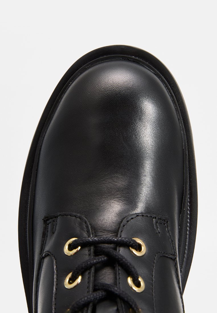 Stivale in pelle nera con punta arrotondata, caratterizzato da occhielli dorati, lacci neri e una texture liscia e lucida. Suola in gomma resistente.