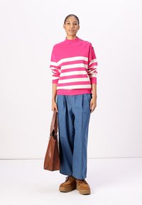 Pull en tricot rayé rose et blanc avec un col montant, associé à un pantalon en denim bleu ample et des chaussures à plateforme beiges. Sac fourre-tout marron à la main.