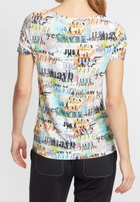 Kortärmad t-shirt med rund hals i flerfärgad tyg som har upprepade textmönster i olika typsnitt. Lätt och slät textur.