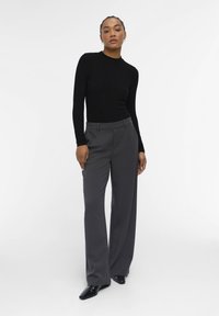 Black ribbed long-sleeve top paired with gray wide-leg trousers. The top features a high neck, while pants have a smooth fabric finish and neutral color.