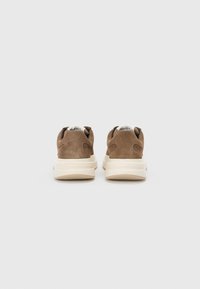 Brown suede sneakers with a cushioned cream sole. The back features cutouts and a smooth neckline for comfort. Minimalistic design.