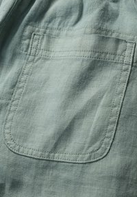 Světle zelená látka s texturovaným povrchem, obsahující jednu obdélníkovou náprsní kapsu a kontrastní švy podél okrajů.