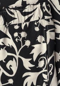 Tissu noir avec motifs floraux et feuillus blancs montrant une taille et une poche latérale.
