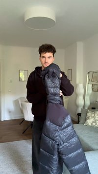 Juodas paminkštintas švarkas su blizgiu paviršiumi, turintis tekstūrinius panele ir kapotą. Vidaus spalva kontrastuoja su išorine.