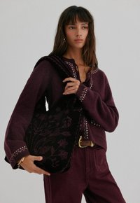 Zwarte borduurtas met bloemenpatronen, gecombineerd met een bordeauxkleurige gebreide trui met witte stikdetails.