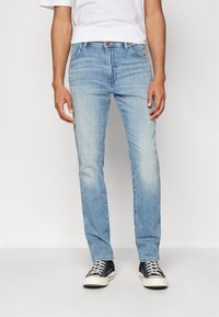 Slim-fit svetlo modri jeans z diskretnim zbledelostjo in klasičnim petim žepnim dizajnom, v kombinaciji s črnimi supergami z belimi detajli.