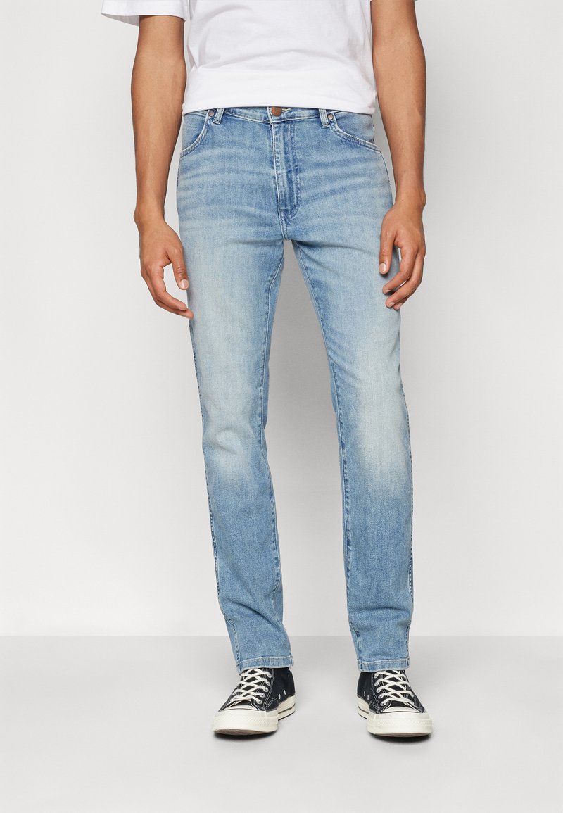 Slim-fit svetlo modri jeans z diskretnim zbledelostjo in klasičnim petim žepnim dizajnom, v kombinaciji s črnimi supergami z belimi detajli.
