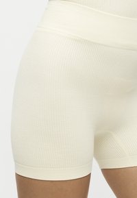 Κοντινό πλάνο ενός ατόμου που φοράει εκρού υφασμάτινες πλεκτές σορτς με ψηλή μέση και φαρδιά ζώνη.