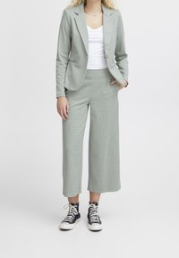 Světle zelený kostkovaný oblek s dokonale padnoucím sako a širokými kalhotami, doplněný bílým topem a černými vysokými teniskami.