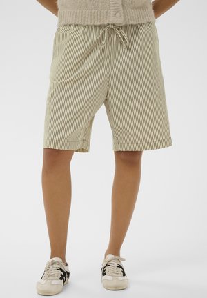 Ben klædt i beige og hvide lodrette stribede shorts med snøre, parret med hvide sneakers med sorte detaljer på en hvid baggrund.