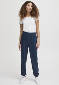 Mørkeblå elastiske bukser med tætsiddende manchetter, parret med en hvid t-shirt med rund hals og hvide sneakers. Glat tekstur, afslappet pasform.