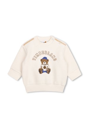 Babytrui in crèmekleur met een teddybeer die een blauwe hoed en laarzen draagt, en het woord "Timberland" in een boog boven de beer.