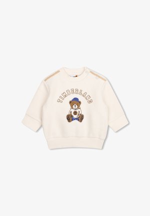 Babytrui in crèmekleur met een teddybeer die een blauwe hoed en laarzen draagt, en het woord "Timberland" in een boog boven de beer.