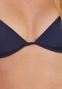 Dunkelblauer Bikini-Oberteil mit dreieckiger Form, gerafftem Stoff an den Seiten, zentralem Verbindungsstück und glattem, elastischem Material.
