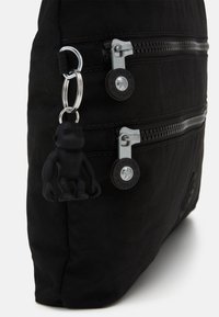 Schwarze Nylon-Tasche mit zwei Reißverschlusstaschen, silbernen Beschlägen und einem schwarzen Affen-Schlüsselanhänger. Glatte Textur, rechteckige Form.
