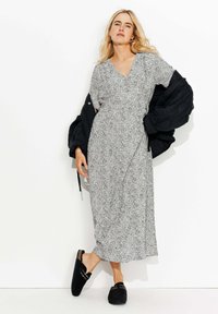 Robe maxi imprimée en noir et blanc avec un décollet�é en V et des manches courtes, associée à une veste matelassée noire et des chaussures noires à enfiler.