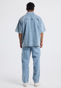 Vaaleansininen farkkupaita, jossa on rento leikkaus, lyhyet hihat ja kaulus, yhdistettynä samanvärisiin vaaleansinisiin farkkuihin.