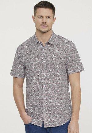 Chemise à manches courtes, blanche, avec un motif tacheté rouge et noir. Dotée d'un col et d'une patte de boutonnage à l'avant. Design décontracté.