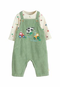 Salopette en velours côtelé vert avec des boutons en bois, ornée de motifs brodés de tracteurs et de vaches. Chemise à manches longues couleur crème avec des motifs de véhicules colorés.
