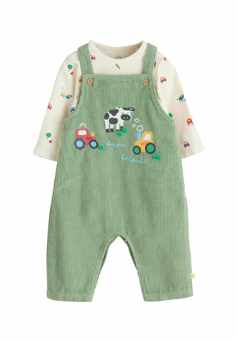 Grüne Corduroy-Latzhosen mit gestickten Motiven von Traktor und Kuh, kombiniert mit einem cremefarbenen Langarmshirt, das bunte Fahrzeugmuster zeigt.