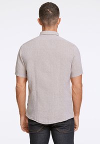 Camisetta a maniche corte, grigia chiara, con tessuto testurizzato, colletto e orlo dritto, abbinata a jeans scuri. Vista posteriore su uno sfondo uniforme.