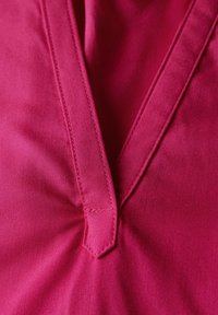 Tessuto rosa con una superficie liscia, caratterizzato da un design a scollo a V e cuciture rinforzate per una maggiore durata.