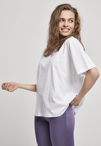 Biela bavlnená tričko s krátkymi rukávmi a voľným strihom, doplnené fialovými legínami. Oblečenie má mäkkú textúru a ležérny dizajn.