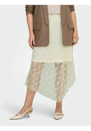 Femme portant une jupe midi en dentelle crème transparente, un blazer beige avec manches retroussées et des chaussures slingbacks crème à talons bas.