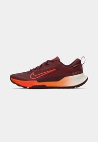 Zapatilla de correr Nike con parte superior de malla color marrón oscuro, acentos naranjas y una suela texturizada. El diseño incluye una lengüeta y un sistema de cordones.