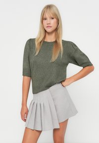 Pull en maille vert olive à manches courtes et col rond, assorti à une jupe plissée gris clair. Tissu texturé et coupe ajustée.