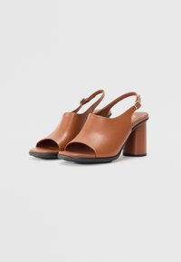 Sandalias de tacón abiertas de cuero marrón con una correa en el tobillo y tacón bloque, que presentan una textura suave y un diseño superior curvado.