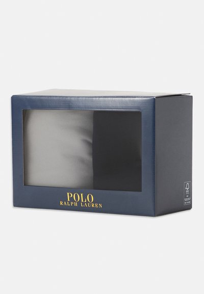 Pakirano stojalo nogavic v prosojni sprednji strani. Temno modra embalaža z zlatim logotipom "POLO RALPH LAUREN". Vsebuje dva para v sivi in črni barvi.