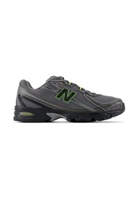Σκούρο γκρι αθλητικό παπούτσι New Balance με μαύρη σόλα, πράσινο λογότυπο "N" και επάνω μέρος από δίχτυ, εμφανίζεται από το πλάι σε λευκό φόντο.