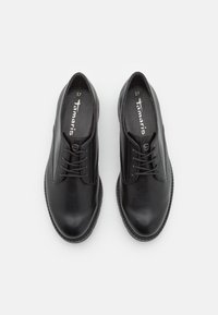 Chaussures en cuir noir avec une texture lisse, bout rond et lacets minimalistes. L'étiquette intérieure indique la taille 37 et la marque "Tamaris."