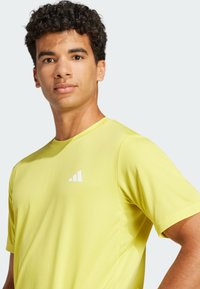 Bright yellow athletic shirt with short sleeves and a textured fabric. Features a white logo on the chest. Simple, modern design.