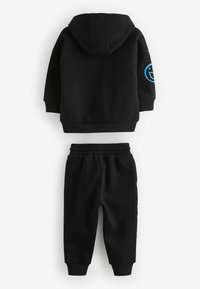 Sort hættetrøje og joggers sæt i bomuldsblanding. Hættetrøjen har blåt logo på ærmet; joggersne har elastisk talje og manchetter ved anklerne.