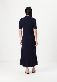 Navy ribbed knit maxi dress with short sleeves and a collar, featuring a fitted silhouette and side slits, paired with light sandals.