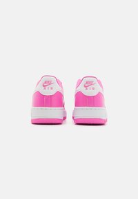 Nike Air -kengät ovat varustettu kirkkaan vaaleanpunaisella synteettisellä päällisellä, jossa on valkoisia yksityiskohtia, sileä pinta sekä kumipohja, jossa on teksturoitu pito-kuvio.