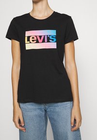 Musta puuvillapaita, jossa on monivärinen "Levi's" -logo vaakasuorassa suorakulmaisessa muodossa. Lyhyet hihat ja ympäri kaula-aukko.
