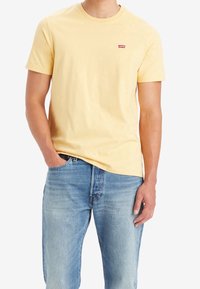 Żółta bawełniana koszulka z okrągłym dekoltem, krótkimi rękawami i małym czerwonym logo Levi's na piersi. Połączona z jasnoniebieskimi dżinsami.