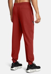 Rote Sporthose mit einem elastischen Bund, seitlichen Taschen und schmal zulaufenden Bündchen, kombiniert mit schwarzen Sportschuhen mit einer weißen Sohle.