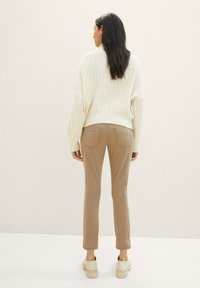 Pull en maille côtelée crème avec des manches ballons associé à un pantalon slim beige. Présente des poches arrière standard et une texture lisse.