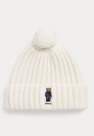 Witte gebreide muts met pompon, met een kleine geborduurde beer in een blauwe outfit en de tekst "POLO" op de omslag.
