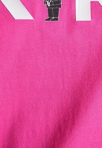 Světlá růžová bavlněná tkanina s malým černým grafickým motivem oblečené postavy a výrazným bílým textem na levé straně. Hladká textura.