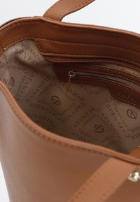 Inredningen av en handväska i tanläder med en dragkedjeficka, prydd med ett tygfoder tryckt med "CAFÉ NOIR"-mönster i beige. Slät textur.