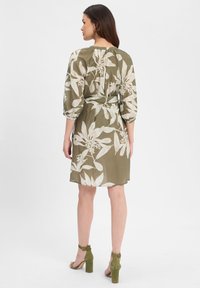 Robe vert olive avec imprimé floral blanc, manches bouffantes 3/4 et taille cintrée. Finition avec un détail de dos en goutte d'eau.
