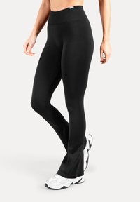 Musta liehuva leggingsit joustavasta kankaasta, jossa korkea vyötärönauha. Yhdistetty valkoisiin lenkkareihin, joissa on sileä, matta pinta.