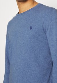 Långärmad blå skjorta i mjukt tyg. Har rund hals, vanlig passform och en liten mörk logotyp på vänster bröst.