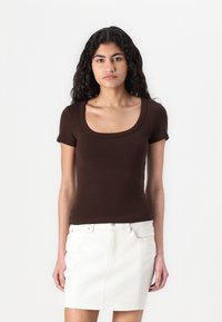 Bruine top met korte mouwen en een vierkante halslijn, gemaakt van zachte stof, gecombineerd met een witte denim rok met zichtbare stiksels en zakken.